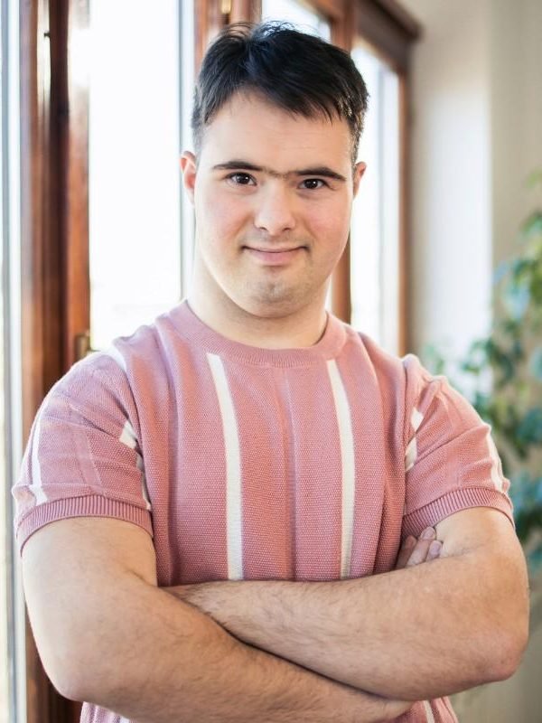 A confident young man with Down syndrome standing with his arms crossed, representing empowerment and self-assurance through NDIS support in Sydney.